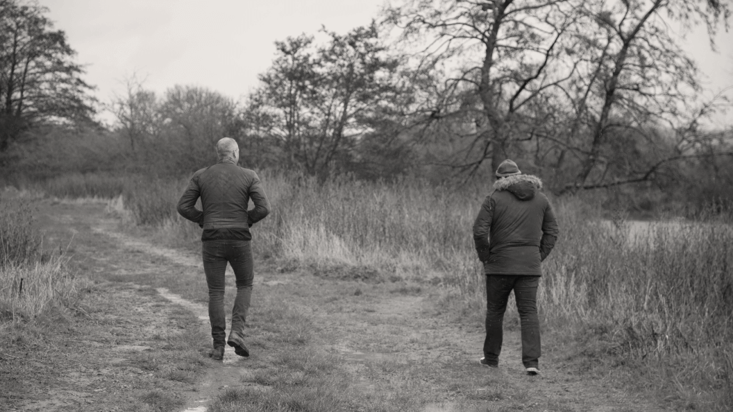 Two male friends with their back to the camera walking down a dirt path.