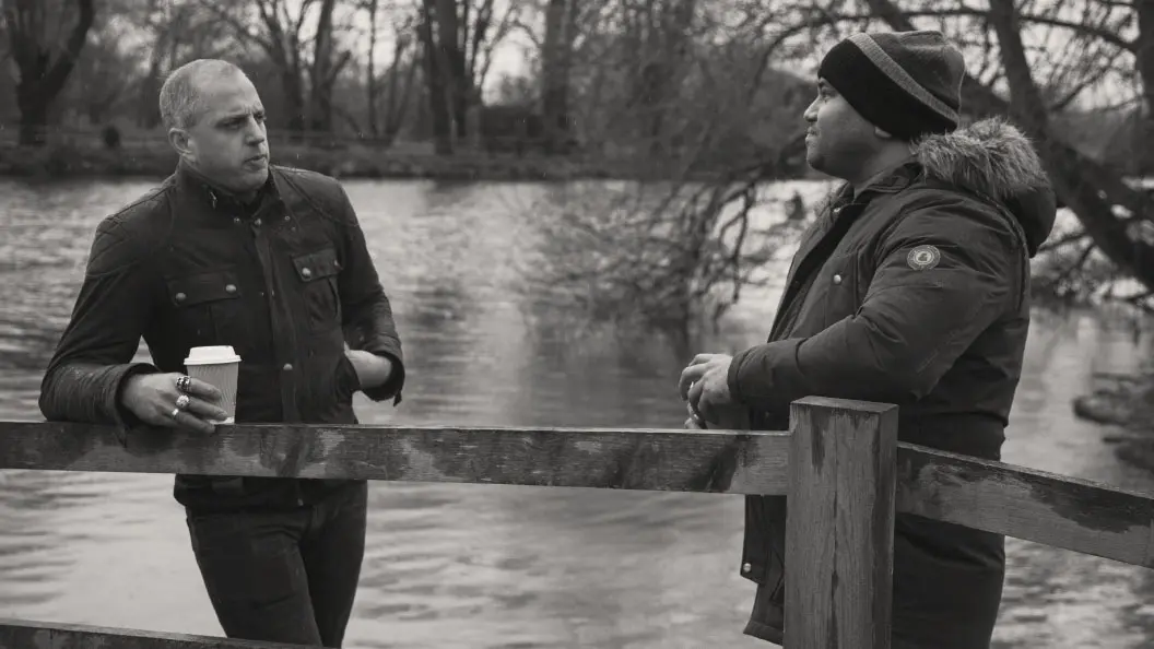 Two men in conversation outdoors next to water