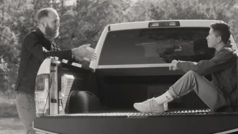 Two young men speaking to each other at the rear of a pick-up truck