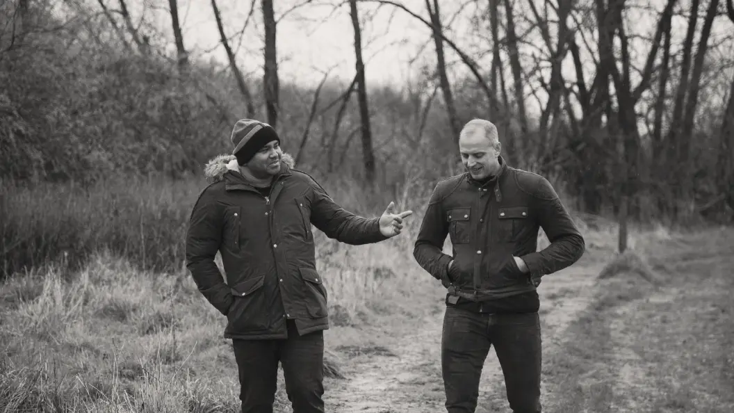 A Black man talking to a white man as they walk together outdoors