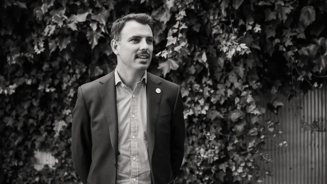 Man in casual suit standing against a wall of vines.