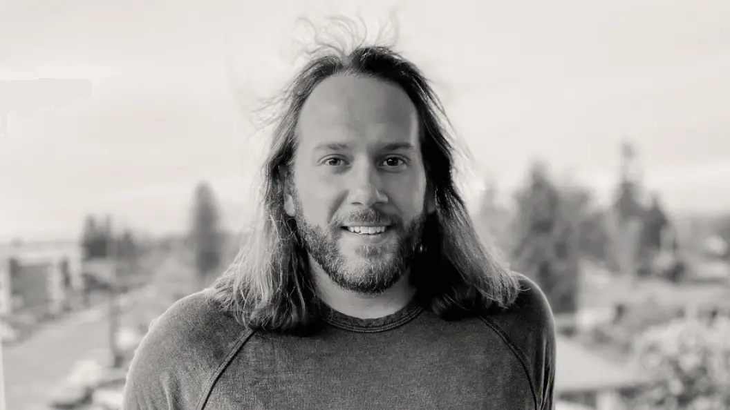 Headshot of young man with a beard and shoulder-length hair 