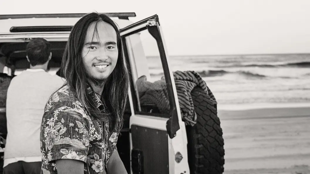 Portrait of man smiling with long hair at the beach, in front of four wheel drive.